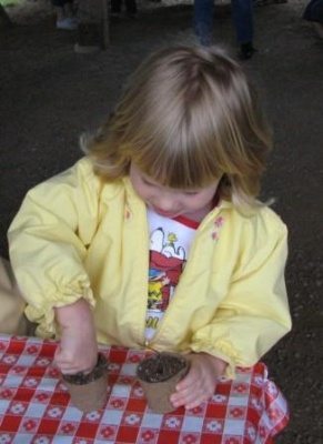 A little girl in a yellow jacket plants sunflower seeds at the Seed planting at the Seed Exchange Social Home School Activity at Great Country Farms in Northern Virginia.