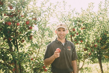 Great Country Farms Pick your own Apple Orchard Manager proudly holds up an apple in the apple orchard at Great Country Farms