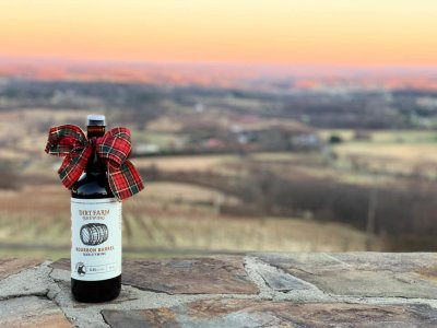 A gift bottle of Dirt Farm Brewing’s Bourbon Barrel Barley wine sits on the stone will with views of Bluemont Virginia