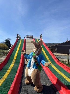the Easter Bunny welcomes guests to Great country farms for Easter Egg Hunts as he stands in front of the Mega Slide.